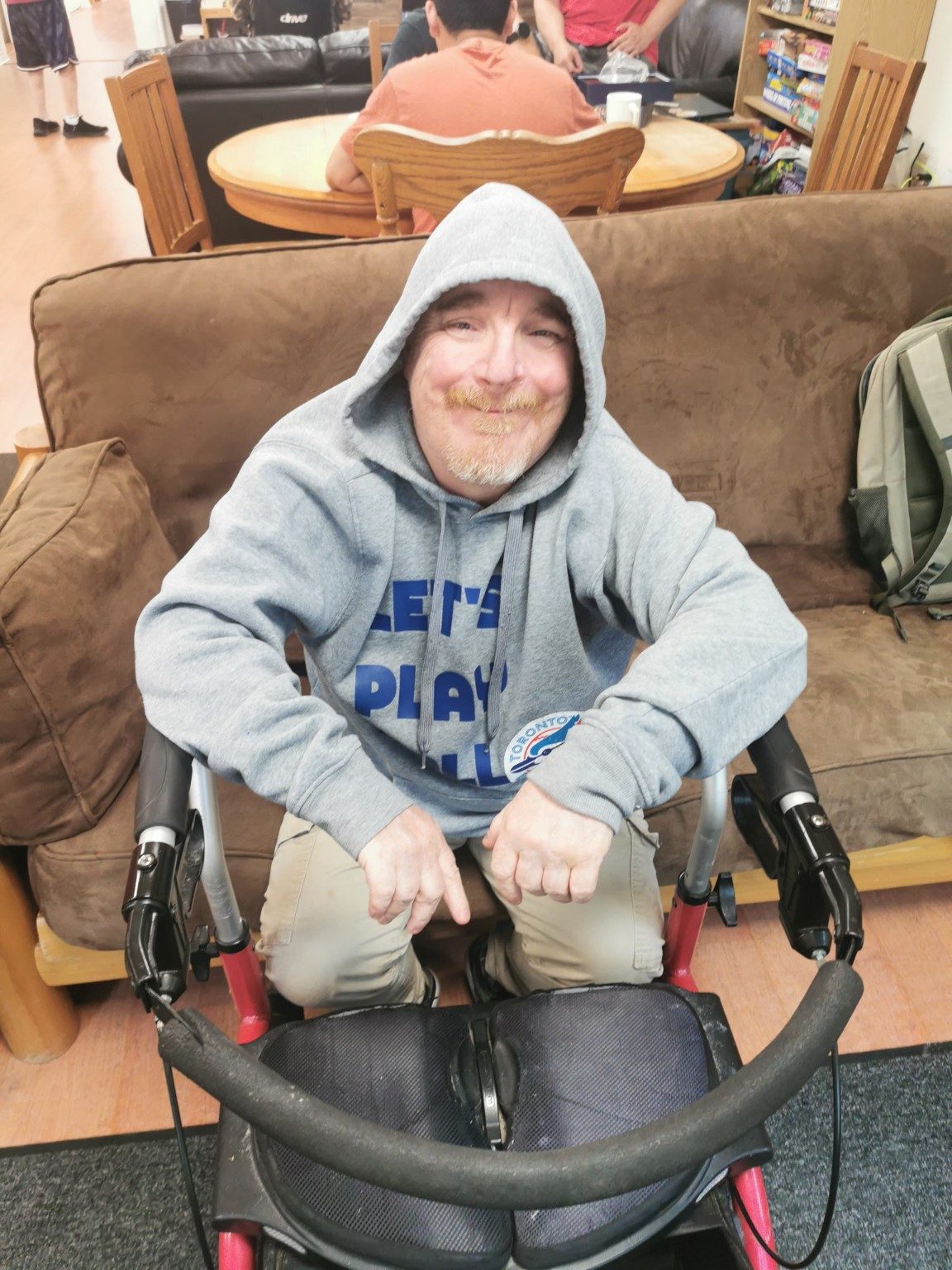 A man smiling while seated beside his rollator in an Access common room